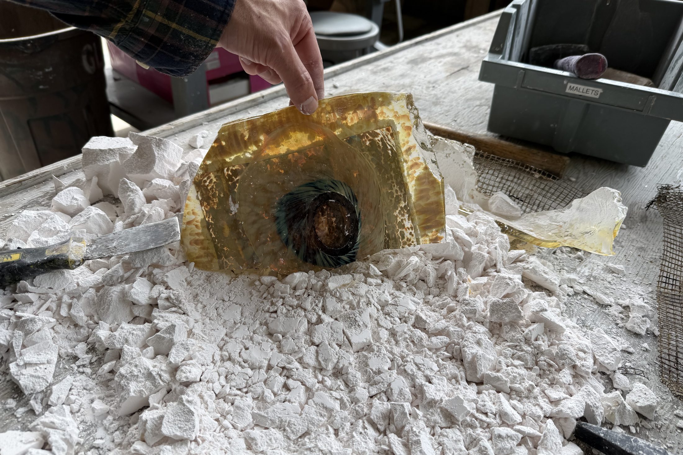 An amber glass casting being lifted out of broken plaster.