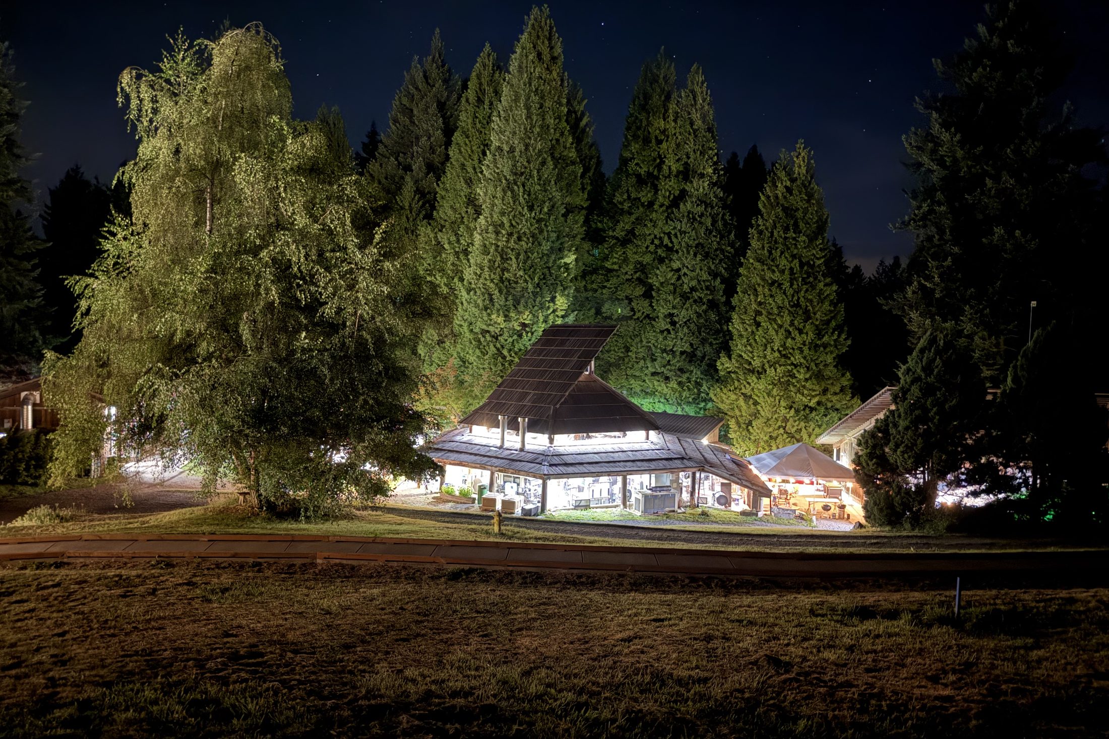 The Pilchuck hot shop lit up at night under tall firs.