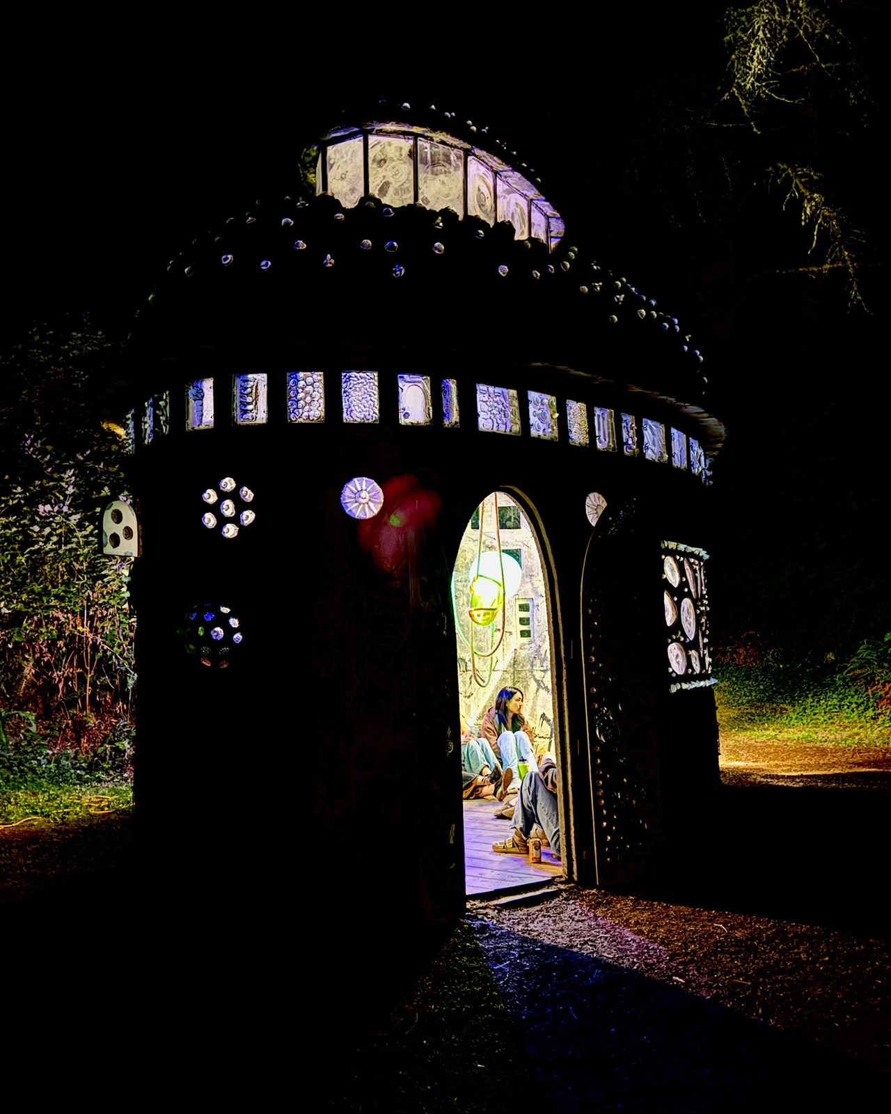 A small round building set with glass, glowing at night on the Pilchuck campus.